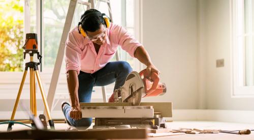 A man is using a circular saw to cut wood for a home building project.