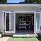 Accessory dwelling unit sits in a backyard with door open revealing interior shelving unit
