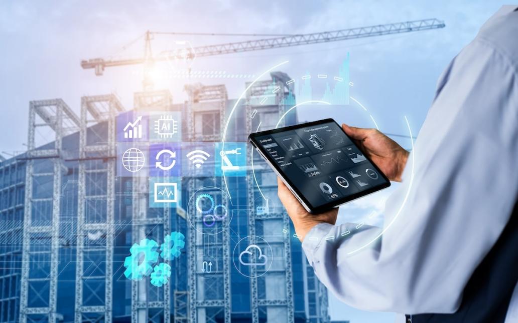 Construction worker at job site looking at tablet, icons floating in front of building that is under construction