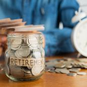 Gen Xer sits at table counting money, in front of them is a clock and a jar labelled "retirement" with coins spilling out