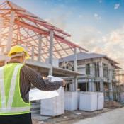 Construction worker looking over plans and staring at framed house in background