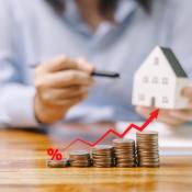 Home price increases represented by stack of coins increasing in value from left to right while man holds model house in background