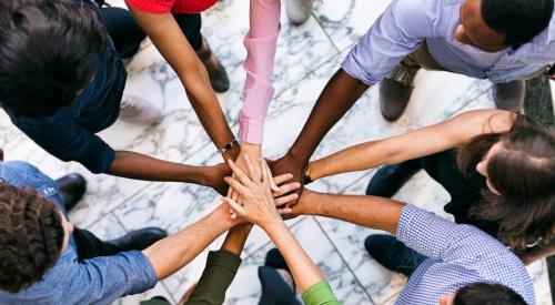 Employees stand in circle with hands on top of one another