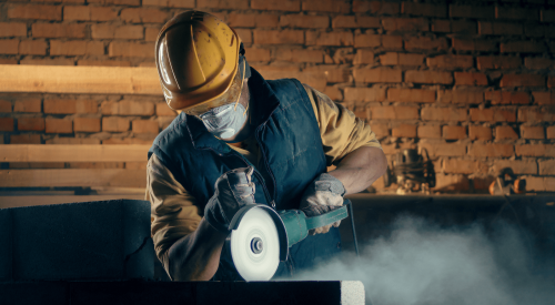 Male construction worker wearing PPE cutting concrete 